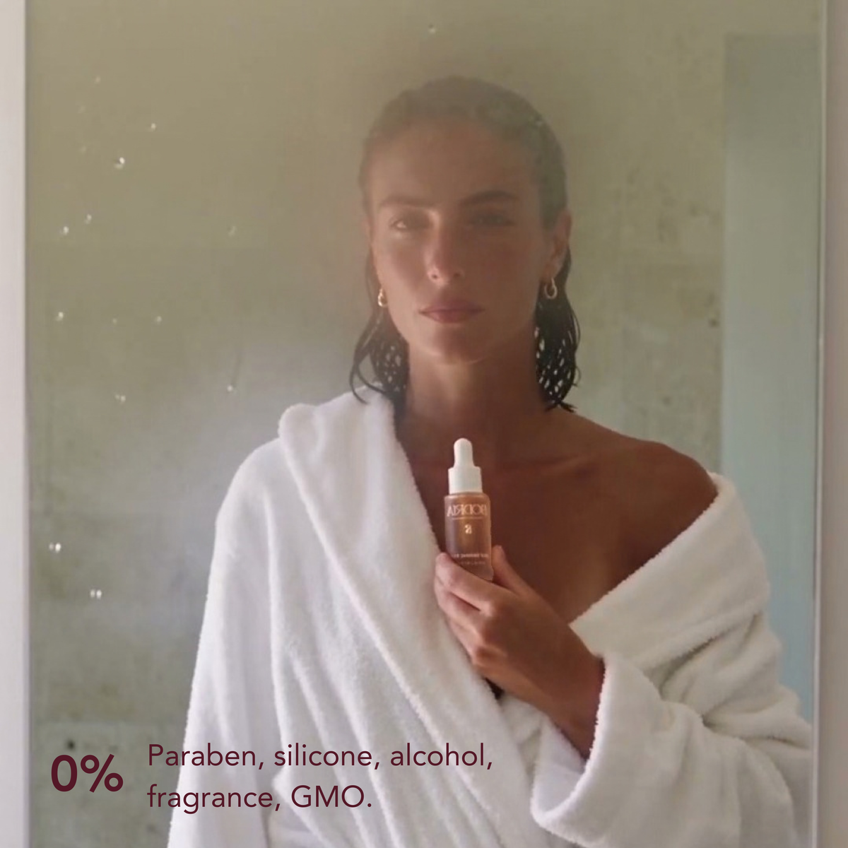 Woman in a white robe holding BODRIA Self Tanning Drop: 0% parabens, silicones, alcohol, fragrance, GMO
